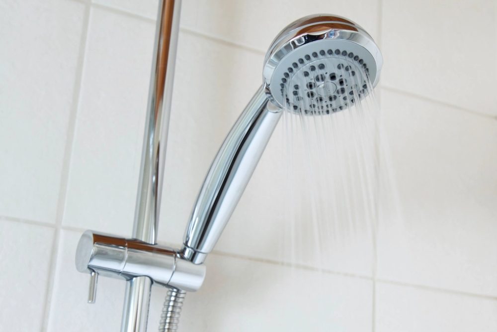 Chrome handheld shower head spraying water in a white-tiled bathroom